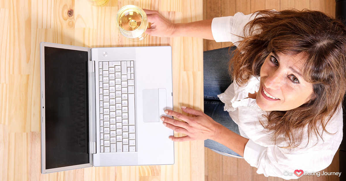 Mature woman with a glass of white wine in front of the laptop